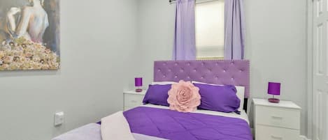 Une chambre à coucher avec un lit, des tables de chevet, une fenêtre avec des rideaux, un tableau au mur et un plateau avec des pommes et du jus.
