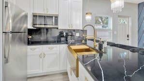 A modern kitchen with white cabinets, stainless steel appliances, a black countertop, gold handles, and a chandelier. - 2 Bed Oasis 10 Minutes to Downtown (tampa)