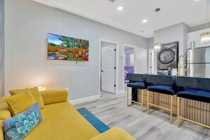 A modern living room with a sofa, a painting, and a kitchen area with a washing machine. - 2 Bed Oasis 10 Minutes to Downtown (tampa)