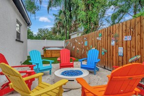 Ein Garten mit Holzzaun, bunten Adirondack-Stühlen, einer Feuerstelle und einer Holzterrasse.