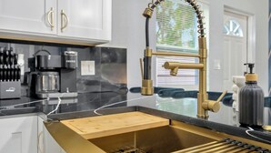 Una cocina moderna con un grifo dorado, una cafetera y una tabla de cortar de madera integrada.