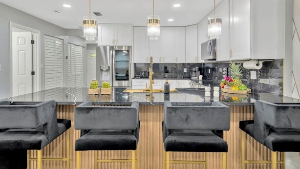 Una cucina moderna con un'isola centrale, sedie nere stile bar e un lampadario.