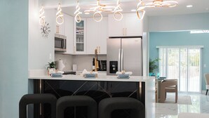 Une cuisine moderne avec des meubles blancs, un réfrigérateur en acier inoxydable et un coin bar doté de chaises noires.