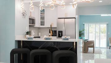 A modern kitchen with white cabinets, a stainless steel refrigerator, and a bar area with black chairs.