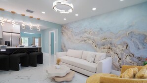 Un salon moderne avec un sol en marbre, un canapé blanc, un fauteuil jaune et une fresque murale originale.