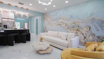 Un salón moderno con suelo de mármol, un sofá blanco, un sillón amarillo y un mural único en la pared.