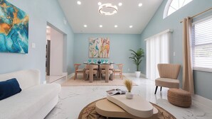 Un salon moderne avec un canapé blanc, un coin repas comprenant une table et des chaises, une grande peinture abstraite et une plante en pot.