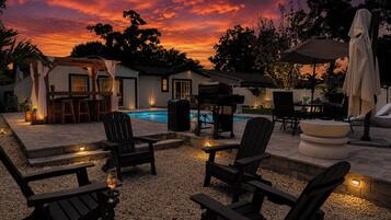 An outdoor patio area with a pool, seating, and a barbecue setup.
