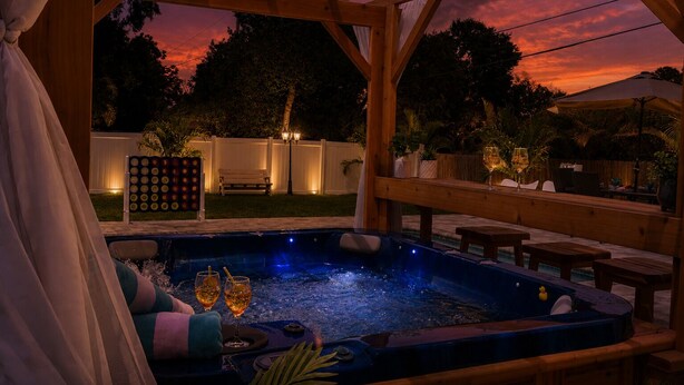 Un bain à remous sous une pergola en bois, offrant une vue sur le coucher de soleil, entouré d’une terrasse et de mobilier d’extérieur.