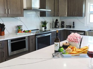 A modern kitchen with stainless steel appliances, a marble countertop, and a variety of food items including bread, grapes, and a bottle of wine. - Lux 4 Bedroom Bayfront Retreat with Hot Tub & Dock (tampa)