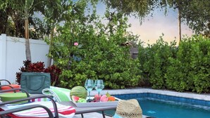A poolside area with lounge chairs, a table with a tray of fruit and drinks, and a hat on one of the chairs. - Stay & Play Downtown Tampa Sleeps 10- HotTub & Bar (tampa)
