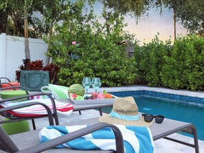 A poolside area with lounge chairs, a table with a tray of fruit and drinks, and a hat on one of the chairs. - Stay & Play Downtown Tampa Sleeps 10- HotTub & Bar (tampa)
