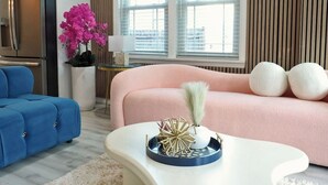 A modern living room with a sofa, a coffee table, a blue armchair, a kitchen area, and a window with blinds. - Stay & Play Downtown Tampa Sleeps 10- HotTub & Bar (tampa)