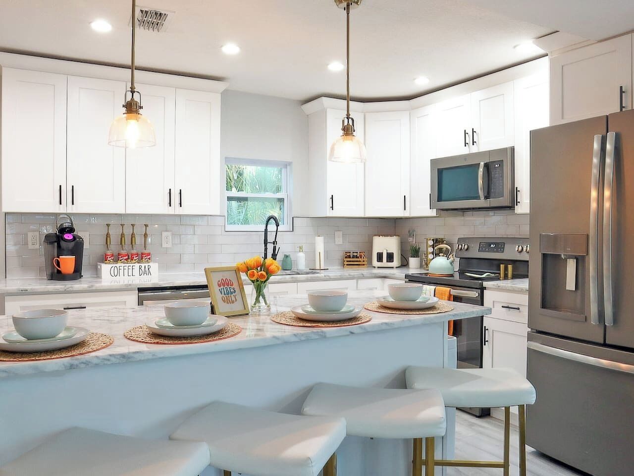 A modern kitchen with white cabinets, stainless steel appliances, a central island with bar seating, and pendant lighting.