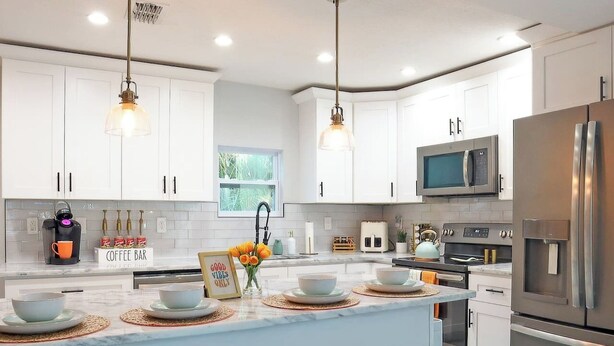 A modern kitchen with white cabinets, stainless steel appliances, a central island with bar seating, and pendant lighting. - Stay & Play Downtown Tampa Sleeps 10- HotTub & Bar (tampa)