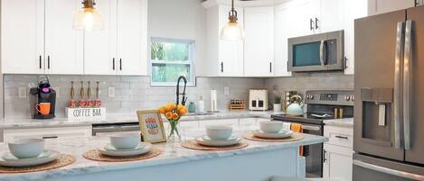 A modern kitchen with white cabinets, stainless steel appliances, a central island with bar seating, and pendant lighting.