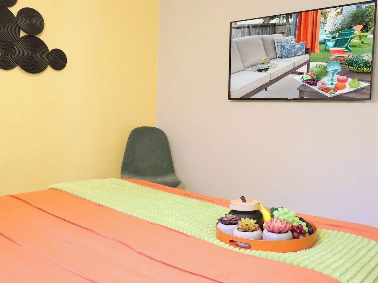 Ein Zimmer mit einem Bett, einem grünen Sessel, einem an der Wand hängenden Bild und einer Obstplatte auf dem Bett.