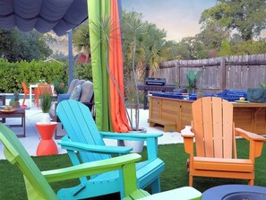 A backyard with outdoor furniture, including two chairs and a table, surrounded by greenery and a wooden fence. - Stay & Play Downtown Tampa Sleeps 10- HotTub & Bar (tampa)