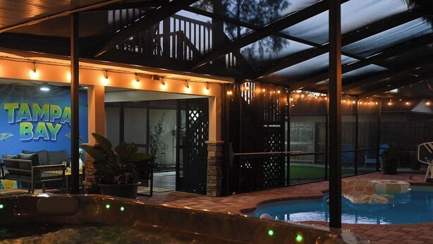 Un área de piscina al aire libre con un jacuzzi, sillas de descanso y un porche cubierto.