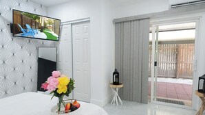 Habitación de hotel con cama, televisor montado en la pared, una mesita con un florero y vistas al exterior a través de una puerta corredera.