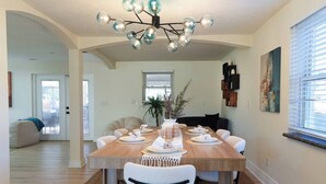 Comedor con mesa de madera dispuesta para cuatro personas, sillas alrededor, una lámpara moderna y una planta en maceta.
