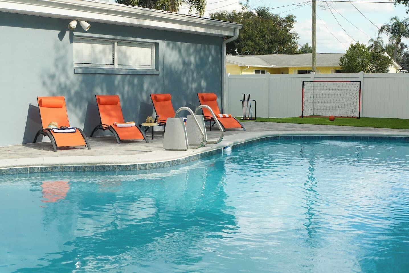 A swimming pool with four orange lounge chairs and a diving board.