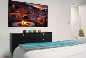 A bedroom with a bed, a black dresser with colorful jars, a painting of a beach scene, and a television displaying a poolside scene. - Tampa High Roller, Relax and Play (Tampa)