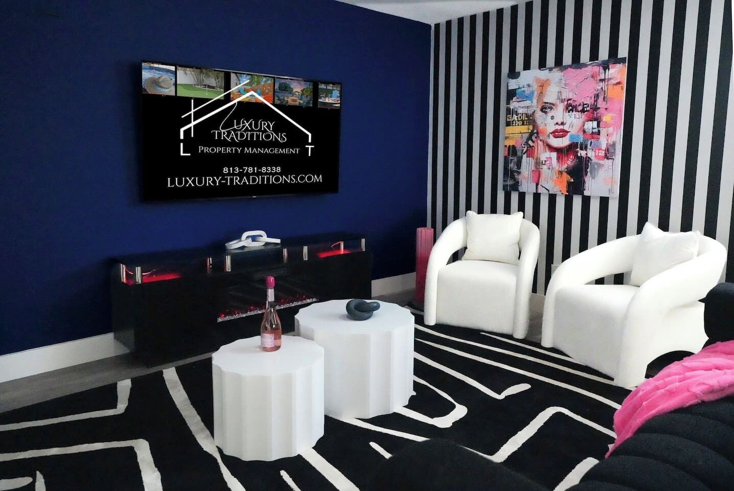 A modern living room with a black and white striped wall, a flat-screen TV, a poster, and two white armchairs.
