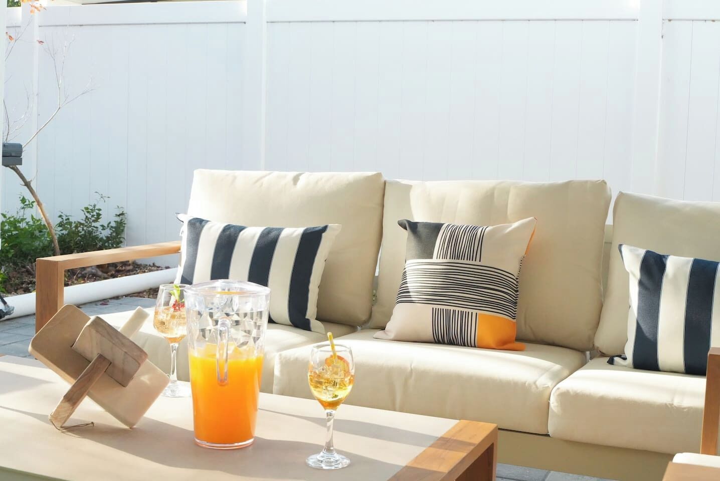 Ein Sitzbereich im Freien mit einer gepolsterten Couch, gestreiften Kissen, einem Holztisch und einer Karaffe Orangensaft.