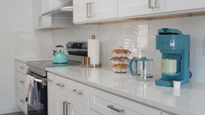 A modern kitchen with white cabinets, a stainless steel range, a teal kettle, a coffee maker, and a tea kettle. - Tampa High Roller, Relax and Play (Tampa)