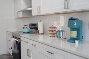 A modern kitchen with white cabinets, a stainless steel range, a teal kettle, a coffee maker, and a tea kettle. - Tampa High Roller, Relax and Play (Tampa)