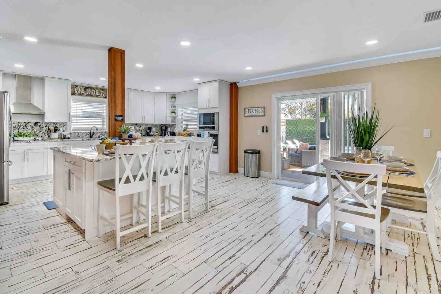Een moderne keuken met witte kasten, een centraal eiland met stoelen, en een eetgedeelte met een tafel en stoelen.