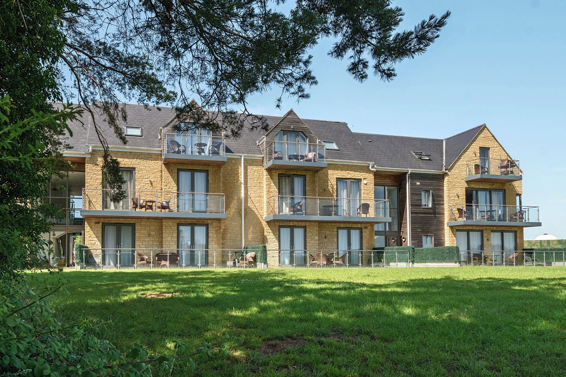 A multi-story residential building with balconies, a grassy lawn, and a clear sky.