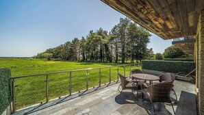 A covered outdoor area with a view of a green field and trees, featuring wicker furniture and a metal railing. - Cotswolds Apartment 2 Sleeps 4 (Chipping Norton)