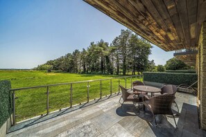 A covered outdoor area with a view of a green field and trees, featuring wicker furniture and a metal railing. - Cotswolds Apartment 2 Sleeps 4 (Chipping Norton)