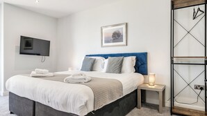 A modern hotel room with a bed, bedside tables, a TV, and a framed picture on the wall. - Cotswolds Apartment 2 Sleeps 4 (Chipping Norton)