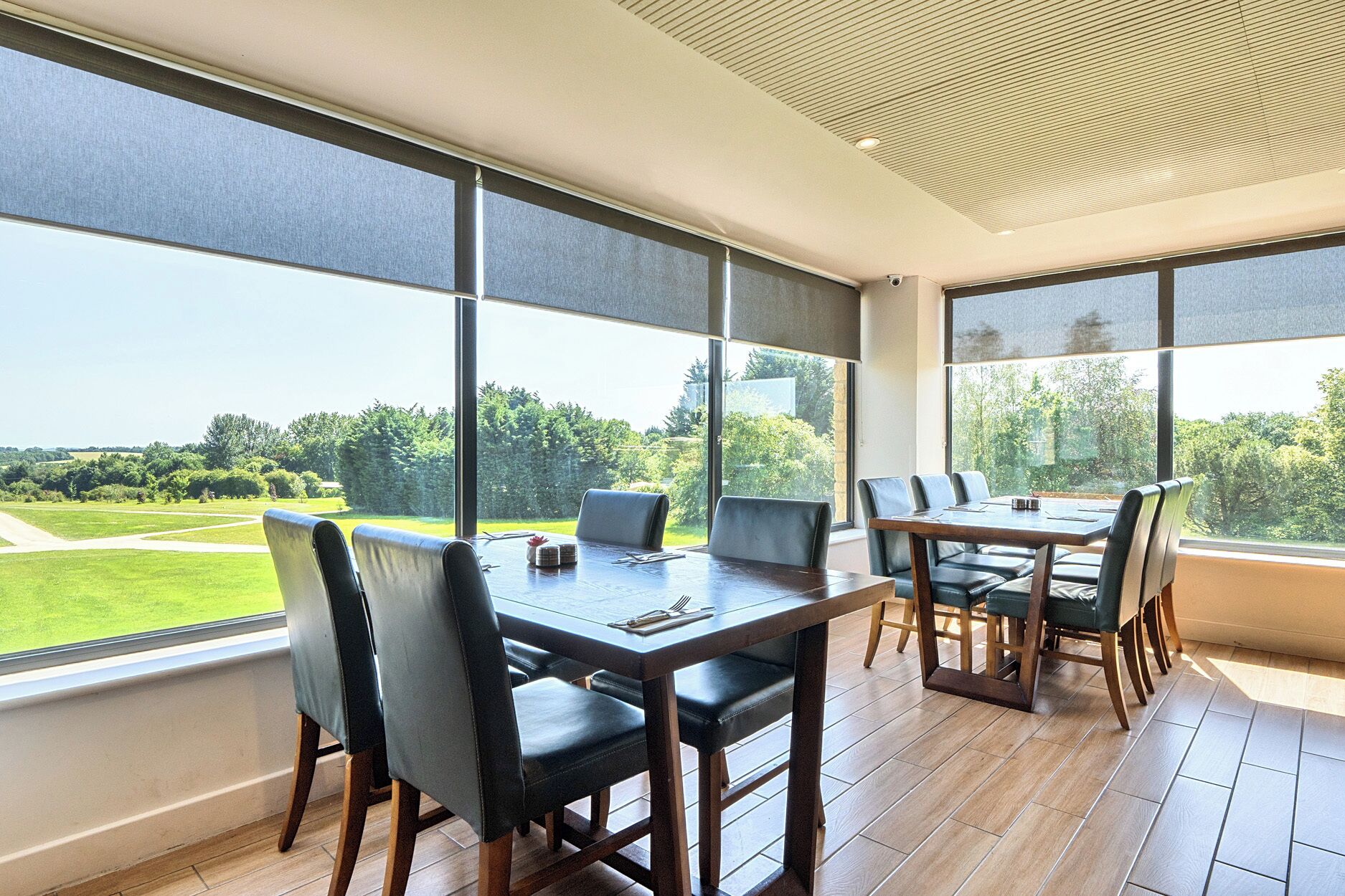 Comedor con una mesa grande y sillas, ventanas amplias con persianas, y vista a un paisaje verde.