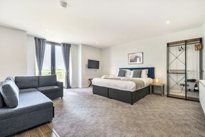 Een moderne hotelkamer met een bank, een bed met blauwe hoofdbord, een televisie en uitzicht op de omgeving.