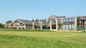 A modern multi-story building with large windows and a flat roof, situated next to a well-maintained grassy area. - Cotswolds Apartment 2 Sleeps 4 (Chipping Norton)