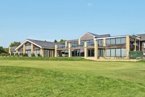 A modern multi-story building with large windows and a flat roof, situated next to a well-maintained grassy area. - Cotswolds Apartment 2 Sleeps 4 (Chipping Norton)