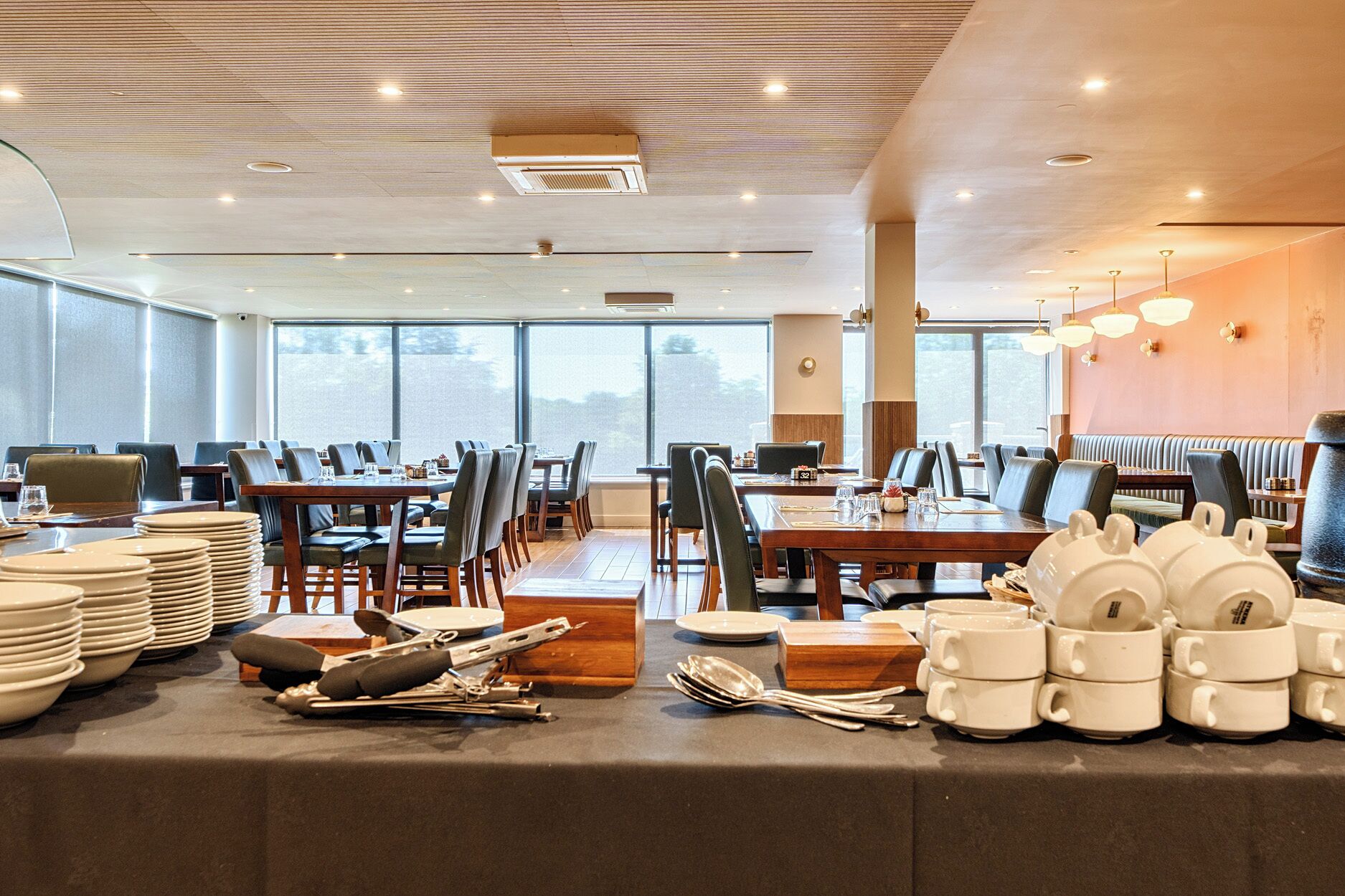 A spacious dining area with multiple tables and chairs, large windows, and a high ceiling with recessed lighting.