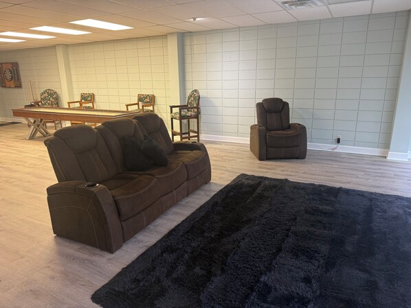 A room with a brown leather sofa, a black furry rug, a recliner, and a dining table with chairs.
