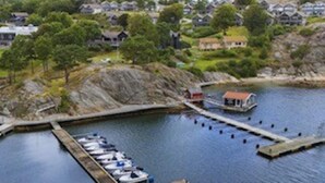 A marina with boats docked, a small building, and houses in the background. - 5 Star Holiday Home in Uddevalla (Uddevalla)