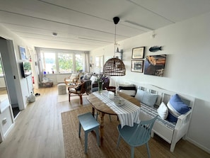 Ein modernes Wohnzimmer mit Essbereich, Holzboden und einem großen Fenster, das für natürliches Licht sorgt.