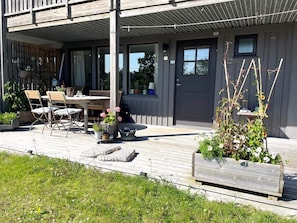 Eine Holzterrasse mit Gartenmöbeln, einer Tür und einem Blumenbeet.