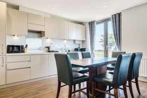 Eine moderne Küche mit weißen Schränken, einem Esstisch mit Stühlen und einem großen Fenster mit Vorhängen.
