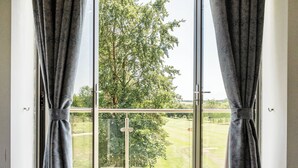 Ein Zimmer mit großem Fenster, Vorhängen und Blick auf eine grüne Landschaft.