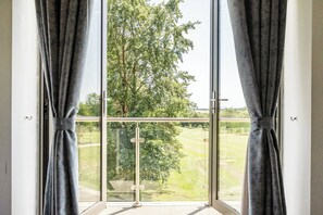 Ein Zimmer mit großem Fenster, Vorhängen und Blick auf eine grüne Landschaft.