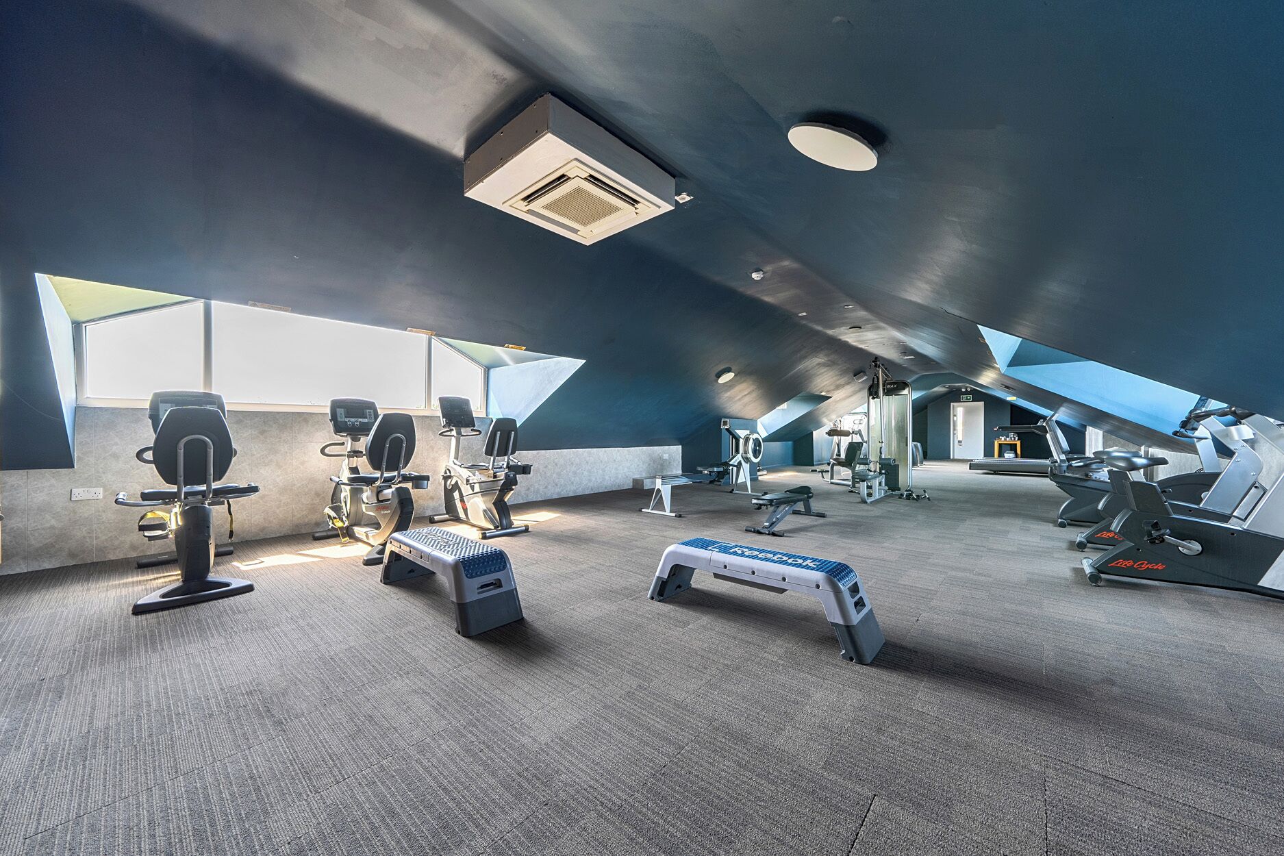 Une salle de sport moderne équipée de divers appareils d’exercice, notamment des tapis de course et des appareils elliptiques.