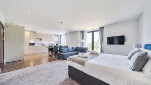 A modern hotel room with a large bed, a flat-screen TV, and a view of the outdoors. - Cotswolds Apartment 3 Sleeps 9 (Chipping Norton)